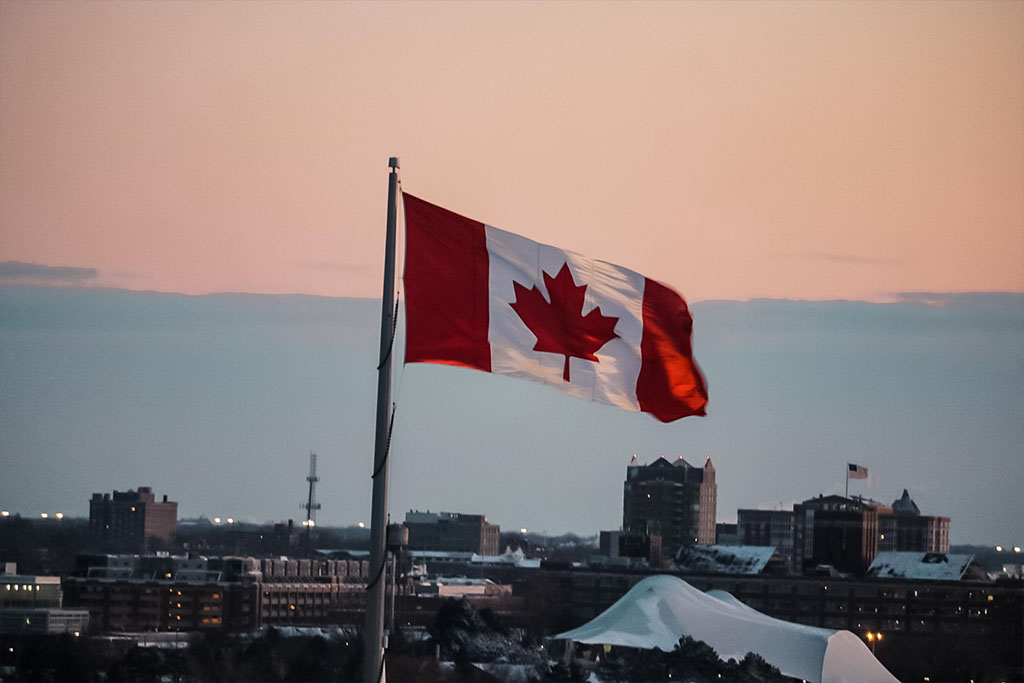 The Canadian flag, with an American city in the background.