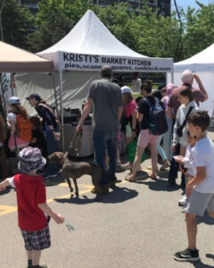 Lots of families visiting a stall at a farmers market.