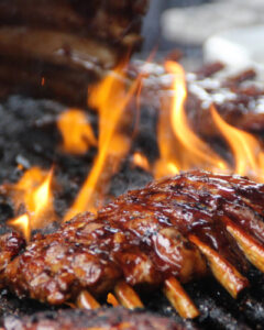 A rack of ribs grilling on the BBQ, with lots of flames. 