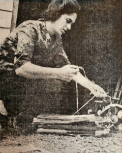 Yellowed newspaper picture of Roberta (Robbie) McGregor, tying string around a stack of cardboard. 